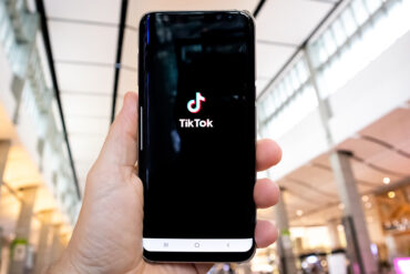 Persoon houdt telefoon in hand met de TikTok applicatie open.