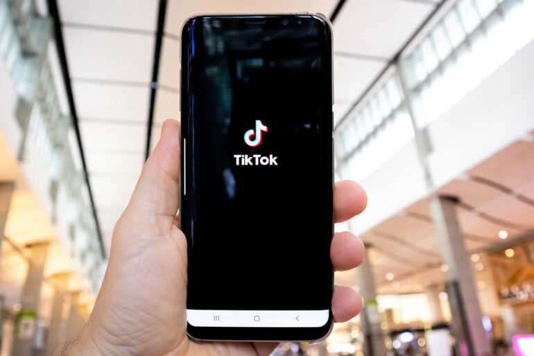 Persoon houdt telefoon in hand met de TikTok applicatie open.