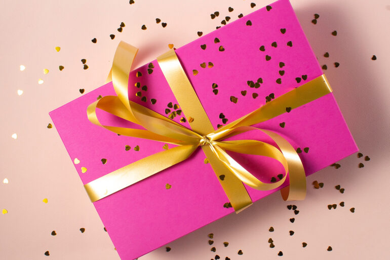 Roze cadeau met gouden strik en hartjes confetti.