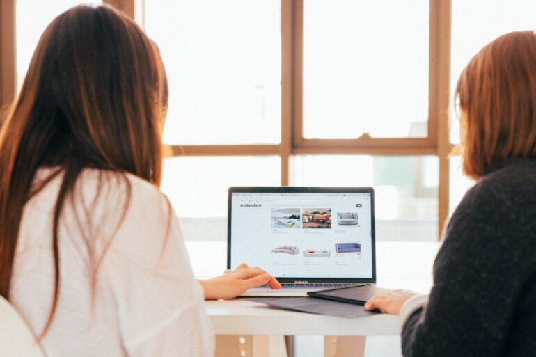 twee vrouwen praten tijdens het kijken naar een website op een laptop