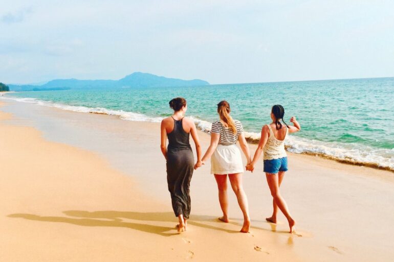drie-vrouwen-lopen-op-kust-onder-blauwe-hemel-