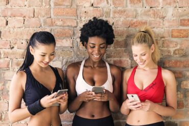 drie-vrouwen-in-sportbeha-s-met-verschillende-kleuren-die-hun-smartphones-vasthouden-en-kijken