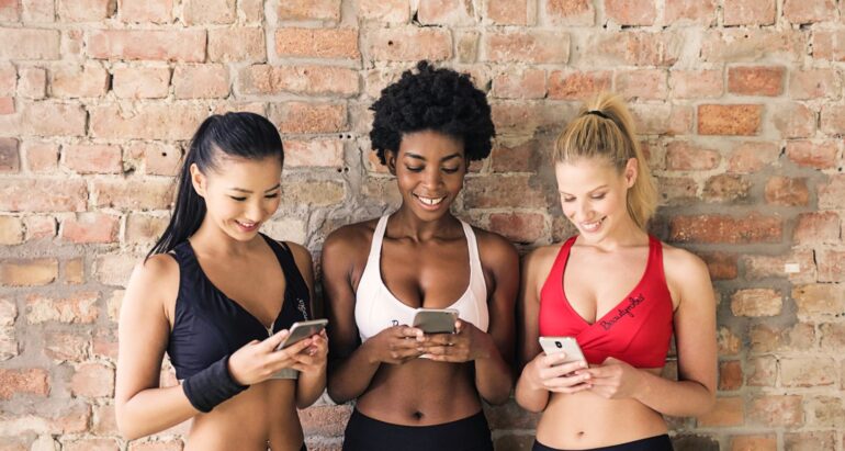 drie-vrouwen-in-sportbeha-s-met-verschillende-kleuren-die-hun-smartphones-vasthouden-en-kijken